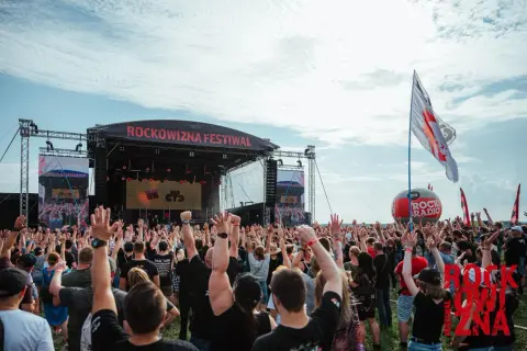 Tłum ludzi z rękami w górze na festiwalu Rockowizna przed sceną.