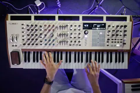 Dłonie grające na białym syntezatorze Arturia PolyBrute 12 z drewnianymi elementami.