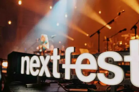 Światła sceny oświetlają napis "next fest" i artystkę grającą na gitarze.