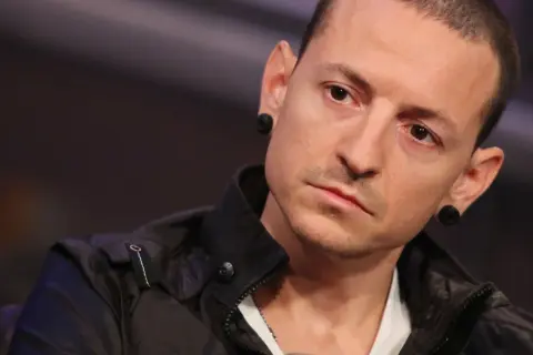 Chester Bennington z Linkin Park, z charakterystycznymi czarnymi tunelami w uszach, w czarnej kurtce.