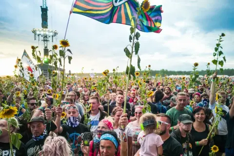 Tłum ludzi na festiwalu Pol'and'Rock trzymający słoneczniki i flagi, z widoczną sceną w tle.