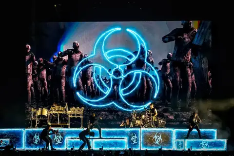 Koncertowy zespół na tle ekranu z symbolem biohazard i zombie.