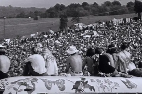 Widok z góry na tłum ludzi na festiwalu Woodstock '69, z kilkoma osobami siedzącymi na ozdobionej ciężarówce.