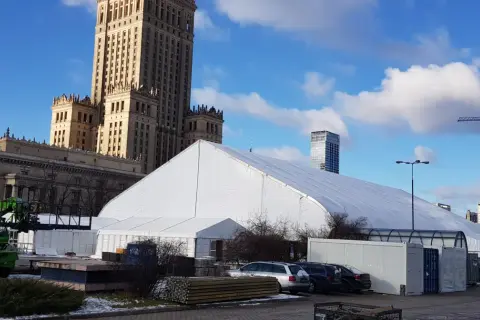 Biały namiot festiwalowy przed Pałacem Kultury w Warszawie, z nowoczesnymi wieżowcami w tle.