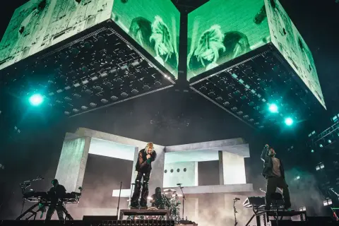 Energetyczny linkin park opener na scenie. Wokalista śpiewa, zespół gra, a nad nimi ogromne ekrany z zielonymi wizualizacjami.