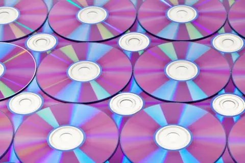 Stos płyt CD/DVD z fioletowo-niebieskimi refleksami, widoczne środkowe otwory.