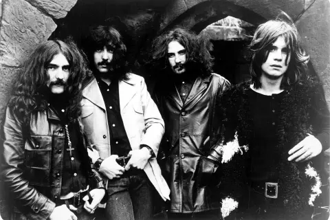 Czterech członków zespołu Black Sabbath pozuje do zdjęcia w mrocznym, kamiennym otoczeniu.