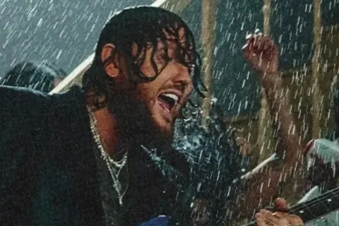 James Arthur śpiewa w deszczu w Warszawie, grając na gitarze.