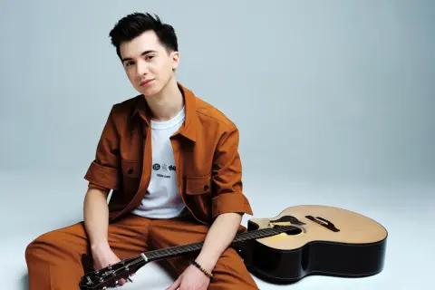 Marcin Patrzałek, młody muzyk, siedzi z gitarą, gotowy na koncert.