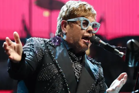 Elton John w błyszczącej marynarce śpiewa na jednym ze swoich niezapomnianych koncertów.