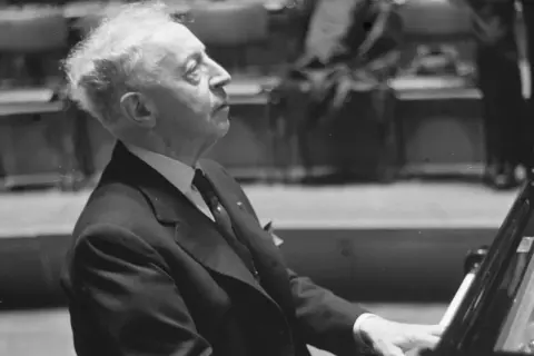 Artysta w garniturze, polski pianista jazzowy, pochyla się nad fortepianem, skupiony na grze.