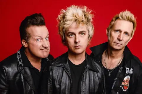 Trzech członków zespołu Green Day na czerwonym tle, w skórzanych kurtkach.