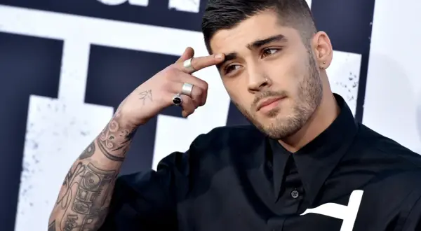 Zayn Malik, były członek One Direction, z tatuażami na ramieniu i palcami ozdobionymi pierścionkami, dotyka czoła.