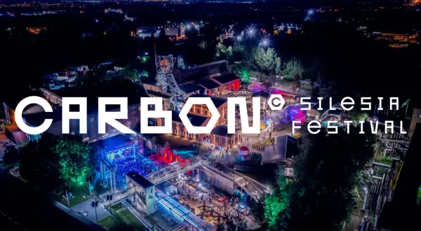 Nocne, oświetlone miasto i teren festiwalowy. Wielkie litery "CARBON Silesia Festival" na pierwszym planie.