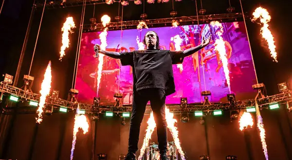Wokalista Falling in Reverse na scenie z płomieniami i ekranem w tle.