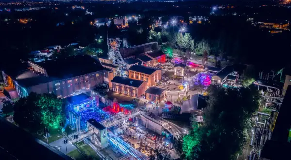 Nocny festiwal z kolorowymi światłami na terenie postindustrialnym. Ludzie bawią się na koncertach i stoiskach. To świetne miejsce na **carbon festival**!
