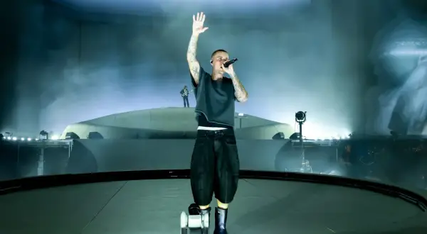 Justin Bieber śpiewa na scenie z podniesioną ręką, otoczony mgłą i światłami.