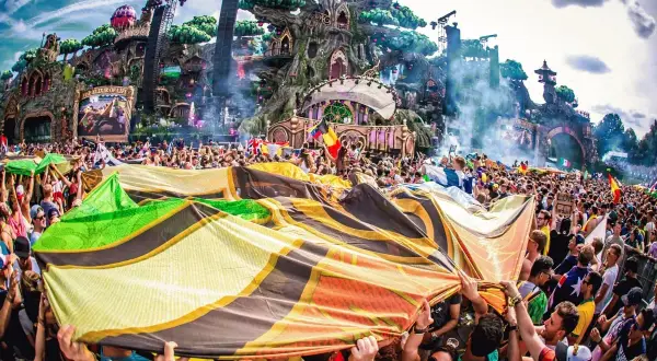 Tłum ludzi na festiwalu Tomorrowland, trzymający kolorową flagę, z imponującą sceną w tle.