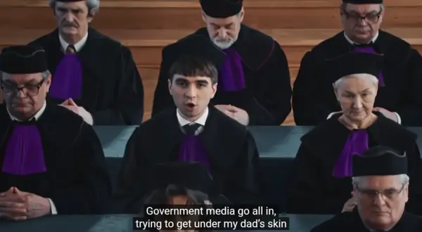 Młody mężczyzna w todze sądowej przemawia przed grupą sędziów w togach.