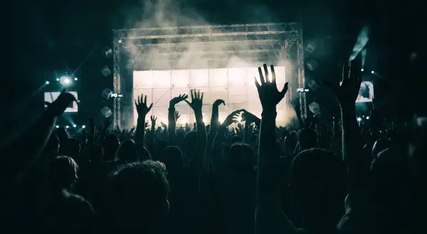 Tłum ludzi z podniesionymi rękami na koncercie przed sceną oświetloną światłami i dymem.
