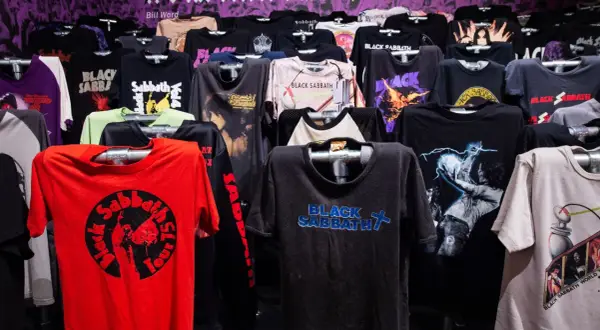 Różnorodne koszulki z logo i grafikami zespołu Black Sabbath wiszące na wieszakach.