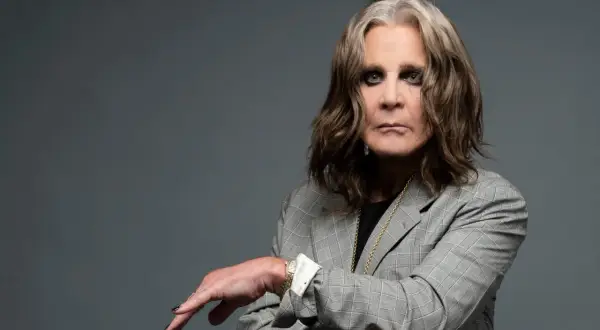 Ozzy Osbourne w szarej marynarce, z charakterystycznym makijażem oczu. Ikona rocka, której ozzy osbourne utwory wciąż inspirują.