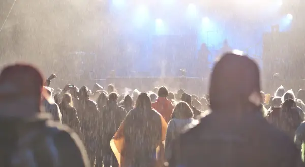 Tłum ludzi na festiwalu w deszczu, widok na scenę z oświetleniem.