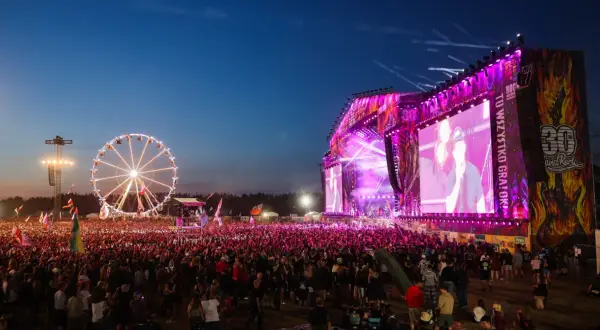 Koncert na Pol'and'Rock Festival z wielkim tłumem, sceną i diabelskim młynem w tle.