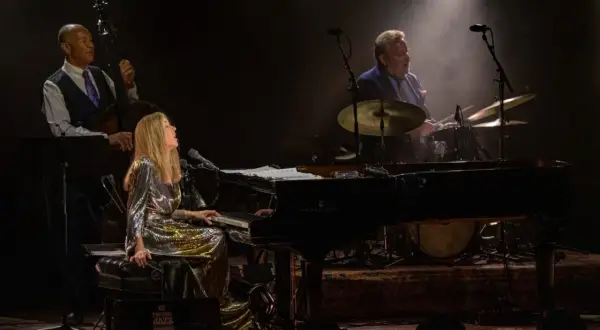 Diana Krall koncert: wokalistka i pianistka w błyszczącej sukni, kontrabasista i perkusista tworzą magiczną atmosferę jazzowego wieczoru.