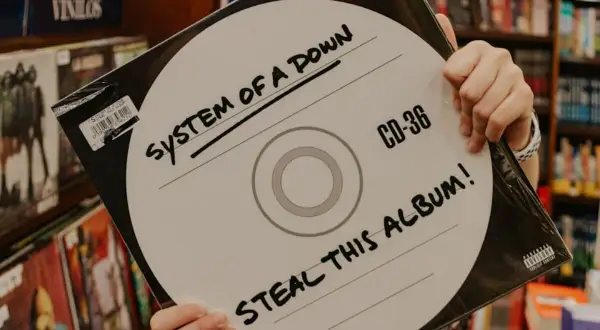 Ręce trzymają okładkę płyty System of a Down "Steal This Album!". Wybór między winylami a CD.