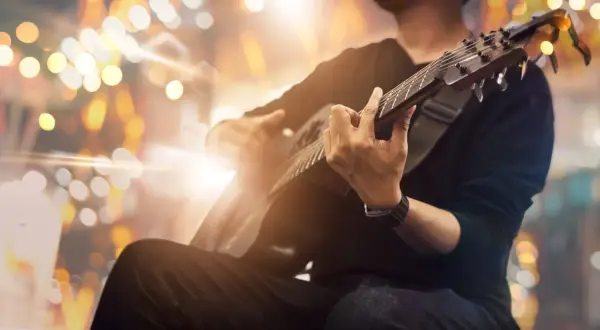 Mężczyzna grający na gitarze akustycznej na tle rozmytych świateł.