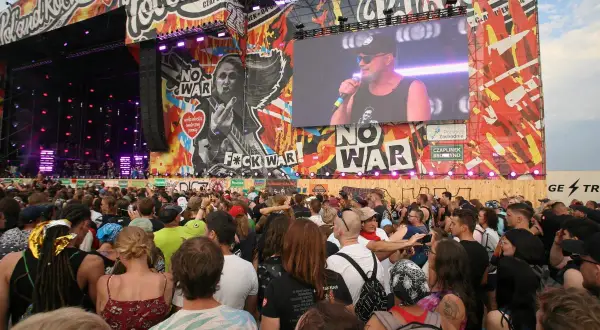 Tłum ludzi na koncercie Pol'and'Rock przed sceną z wielkim ekranem i grafikami.