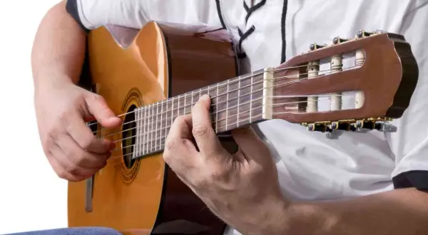 Dłonie grają na gitarze klasycznej, tworząc akordy. To może być najłatwiejsza piosenka na gitarze, którą właśnie ćwiczysz.
