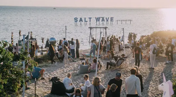 Ludzie na plaży podczas festiwalu Salt Wave, z napisem "SALT WAVE" nad wodą.