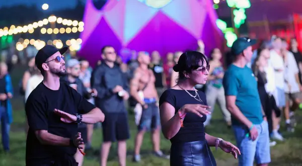 Ludzie tańczący na festiwalu Audioriver w Łodzi, z kolorową scenografią w tle.