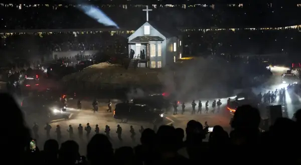 Scena z koncertu Donda 2: biały kościół z krzyżem na dachu, otoczony dymem, ludźmi i samochodami, w blasku reflektorów.
