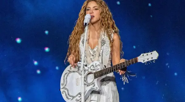 Shakira w Polsce na koncercie, śpiewa z białą gitarą i w białym stroju z frędzlami.