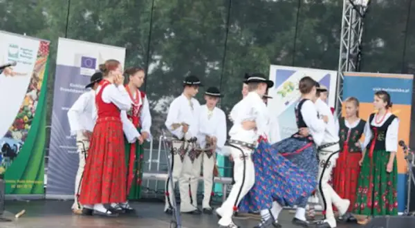 Grupa ludzi w tradycyjnych strojach ludowych tańczy na scenie.