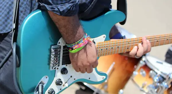Muzyk grający na turkusowej gitarze elektrycznej, w tle bębny.