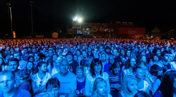 Tłum ludzi na koncercie, oświetlony niebieskim i pomarańczowym światłem. W tle widać banery z logo Energa i Lotos. To prawdziwa inwazja mocy, jak na koncercie Scorpions!