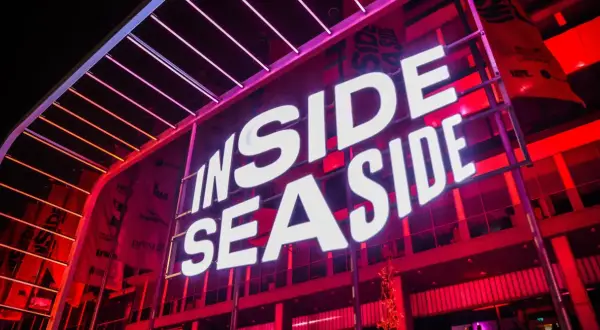 Jasne, oto opis alternatywny:

Duży neon "INSIDE SEASIDE" świeci białym światłem na tle czerwonej, nowoczesnej fasady budynku.