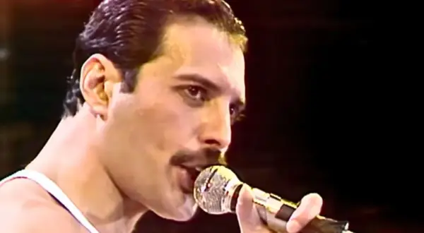 Freddie Mercury śpiewający do mikrofonu na scenie.
