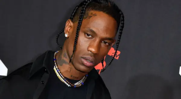 Travis Scott w czarnej koszuli i z warkoczami, z naszyjnikami i tatuażami na szyi.