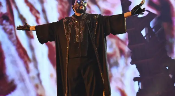 The Weeknd w czarnej, zdobionej masce i stroju, śpiewa na koncercie.