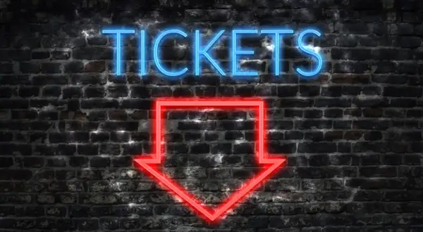 Napis "TICKETS" neonem w kolorze niebieskim i czerwona strzałka w dół na ceglanej ścianie.