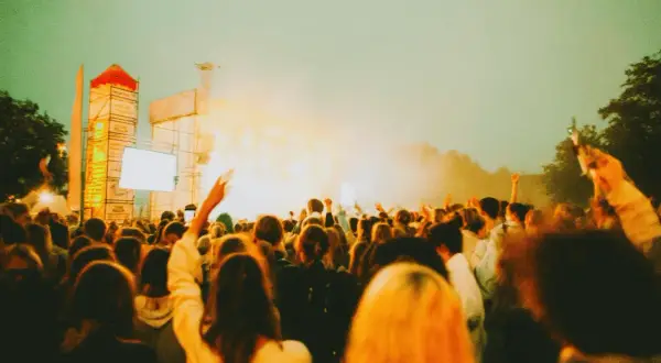 Tłum ludzi na koncercie, uniesione ręce, scena z oświetleniem. Tak wyglądają juwenalia, czyli święto studentów.