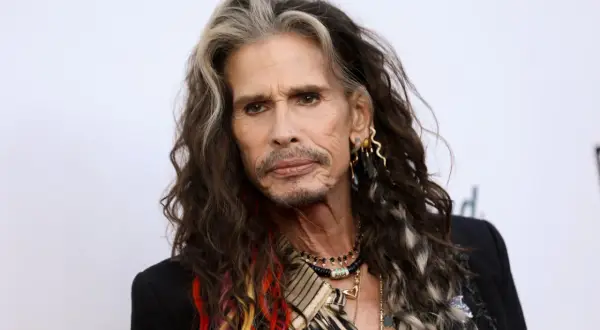 Steven Tyler z kolorowymi pasemkami we włosach, w czarnej marynarce i z biżuterią.