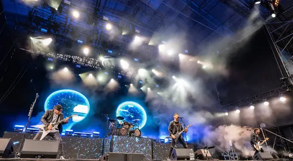 Zespół Bullet For My Valentine gra na scenie podczas koncertu, w tle niebieskie ekrany i światła.