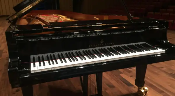 Czarny fortepian Steinway & Sons z otwartą klapą, na drewnianej scenie.