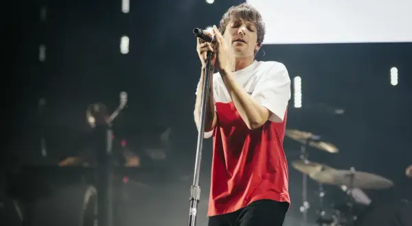 Louis Tomlinson śpiewa na koncercie w Polsce, w czerwono-białej koszulce, z zamkniętymi oczami.
